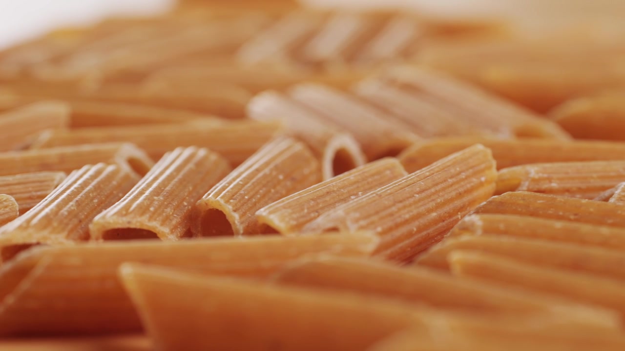 Pasta integrale biologica, maccheroni di semola di grano duro, penne rigate crude in una ciotola di legno. Filmato 4k di alta qualità