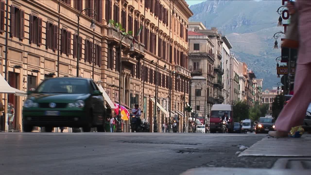 Vecchi edifici fiancheggiano una strada trafficata con veicoli e pedoni che passano a Palermo, Italia.