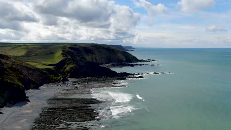 Aerial-coastal-shot-of-the-waves-in-the-sea-at-Spekes-Mill-beach-in-Devon-showing-green-hills