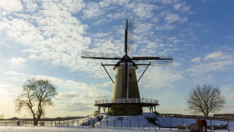 Time-lapse-of-clouds-passing-over-traditional-windmill-in-beautiful-white-winter-rural-landscape---pan-right-to-left