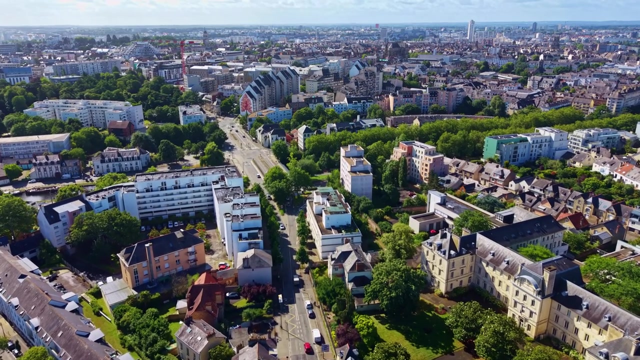 Vorwärts gerichtete Drohnen-Luftaufnahme, die einer Hauptallee durch das Viertel Pontchaillou in Rennes, Frankreich, folgt und Wohngebäude, von Bäumen gesäumte Straßen sowie die Stadtsilhouette in der Ferne zeigt.