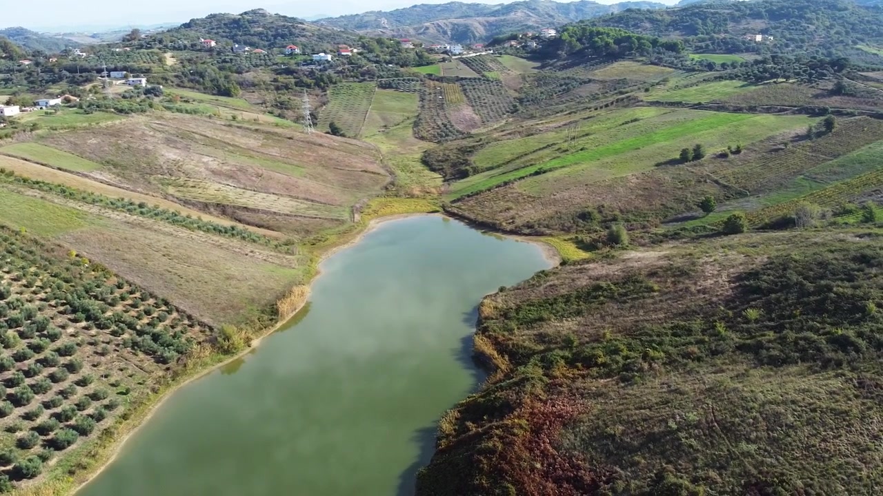 Veduta aerea sopra un piccolo lago nella campagna albanese con campi agricoli e colline