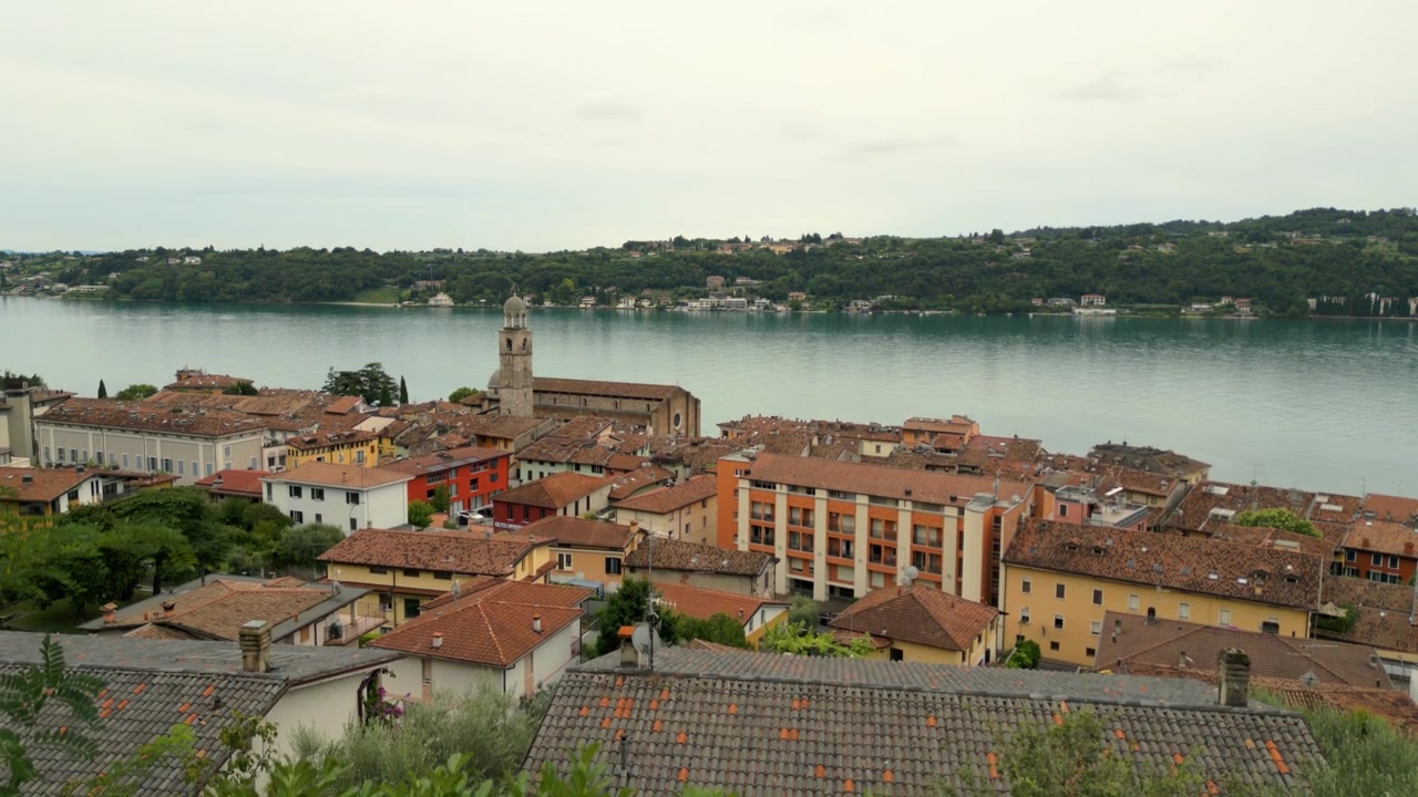 La telecamera si inclina verso il basso dalla vista del lago e della città a densi cespugli verdi in primo piano.