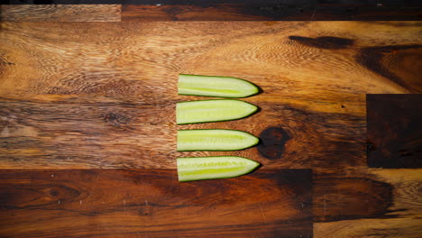 top view of a male hand slicing two pieces of cucumber perpendicular in the middle