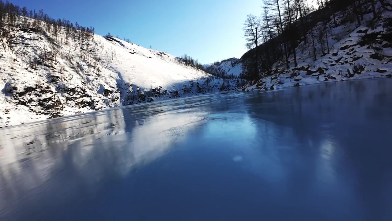 Rauhallinen joki on jään peitossa lumipeitteisessä vuoristomaisemassa. Kohtaus huokuu tyyneyttä ja talvista kauneutta.