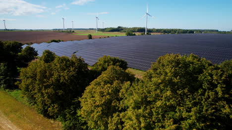 Wind-farm-and-solar-panels-in-nautral-scenery-aerial,-A-huge-renewable-energy-farm-near-trees-and-farmland-by-drone