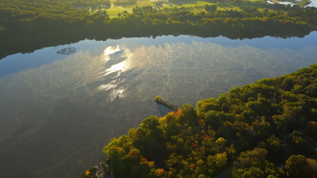Dense fall forest at golden hour sunset along Lake Sequoyah water edge, tranquil seasonal landscape, Wyman Arkansas USA, aerial