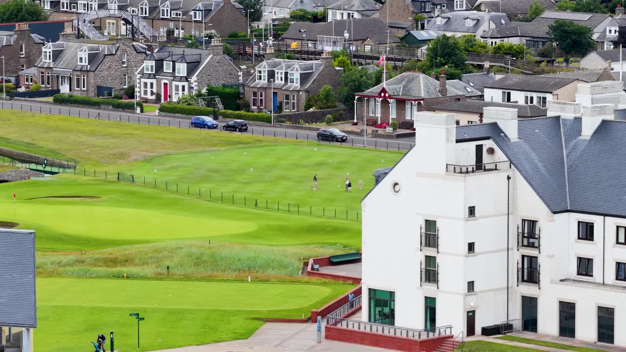 Drone pans across golf course, clubhouse, and town rooftops on a bright summer day