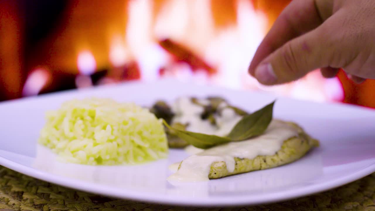 chuleta de pollo con crema y hongos, crema fresca, queso, arroz en un plato cuadrado con un fuego de leña en el fondo