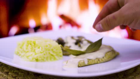 Chuleta-De-Pollo-Con-Nata-Y-Champiñones,-Nata-Fresca,-Queso,-Arroz-En-Un-Plato-Cuadrado-Con-Fuego-De-Leña-Al-Fondo