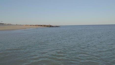 Beautiful-ocean-waters-at-low-altitude-approaching-sea-rocks-in-Ilha-do-Farol,-Portugal-during-a-sunny-day