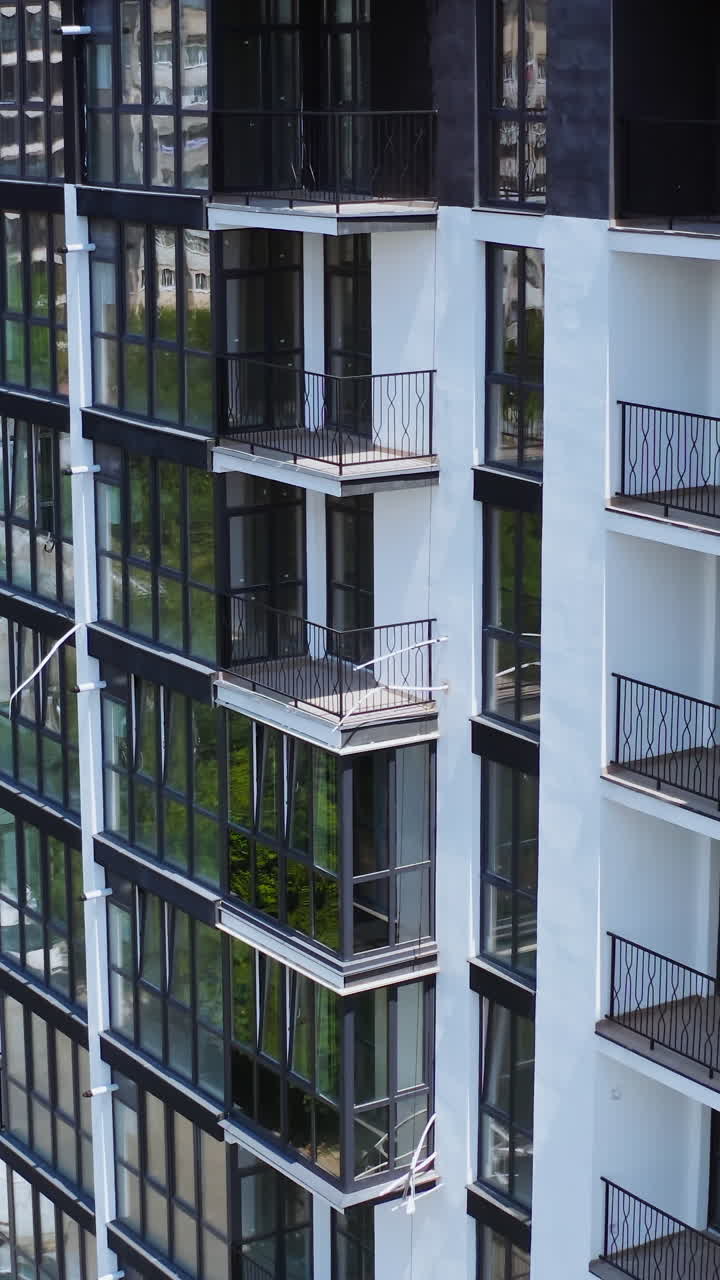 Modern apartment building in new city district. Exterior of a new multi-storey building with beautiful dark windows. Aerial view. Vertical video