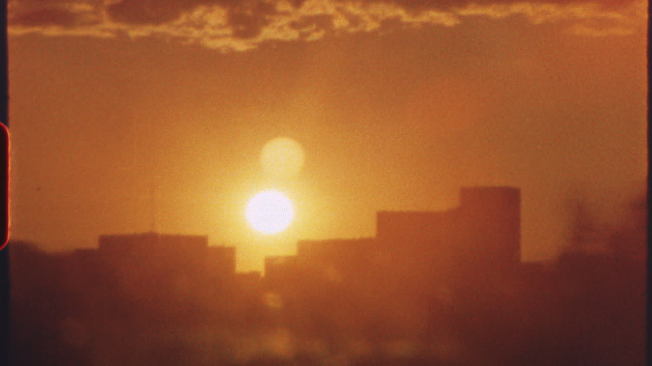 8 mm film - warm golden sunset illuminating urban skyline, vibrant orange hues spreading across cloudy sky during twilight transition