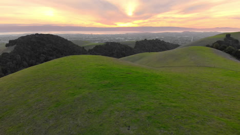 distant sunset behind grey city and green hills, aerial