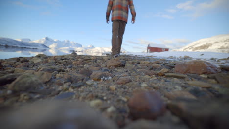 Un-Hombre-Caminando-A-Lo-Largo-De-Un-Shorline-Rocoso-En-Un-Ambiente-De-Invierno-Soleado-Y-Tranquilo,-Cámara-Lenta-Estática-De-ángulo-Bajo