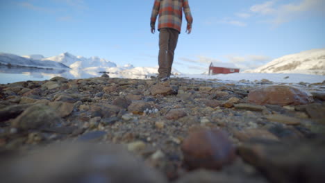 un hombre caminando a lo largo de un shorline rocoso en un ambiente de invierno soleado y tranquilo, cámara lenta estática de ángulo bajo