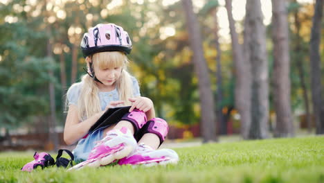 la niña está sentada cerca de la casa disfrutando de la tableta rodada en patines - en su casco y r