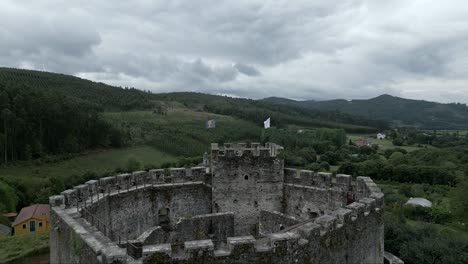 aerial flying over moeche castle tower, revealing san xurxo de moeche parish, spain