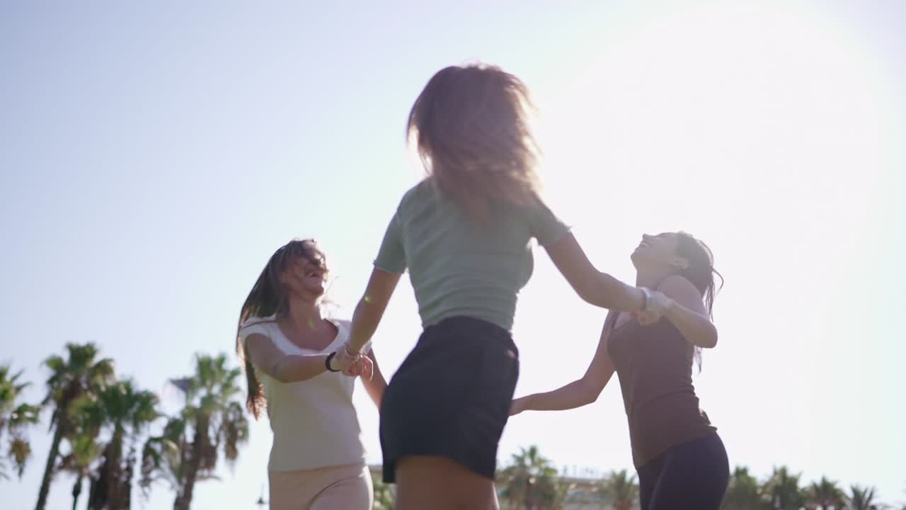 세 명의 여성 친구들이 웃으며 백라이트가 있는 에서 장미를 둘러싸고 놀고 있습니다. 젊은 여성들이 함께 놀고 손을 잡고 달리고 있습니다.