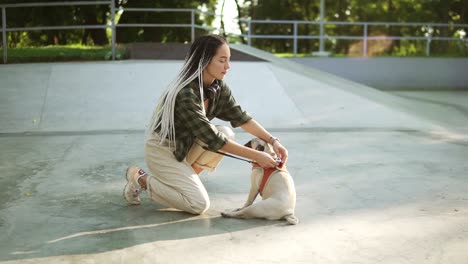 Woman-fastens-a-pug-dog-on-a-leash-in-a-skate-park,-puppy-patiently-waiting