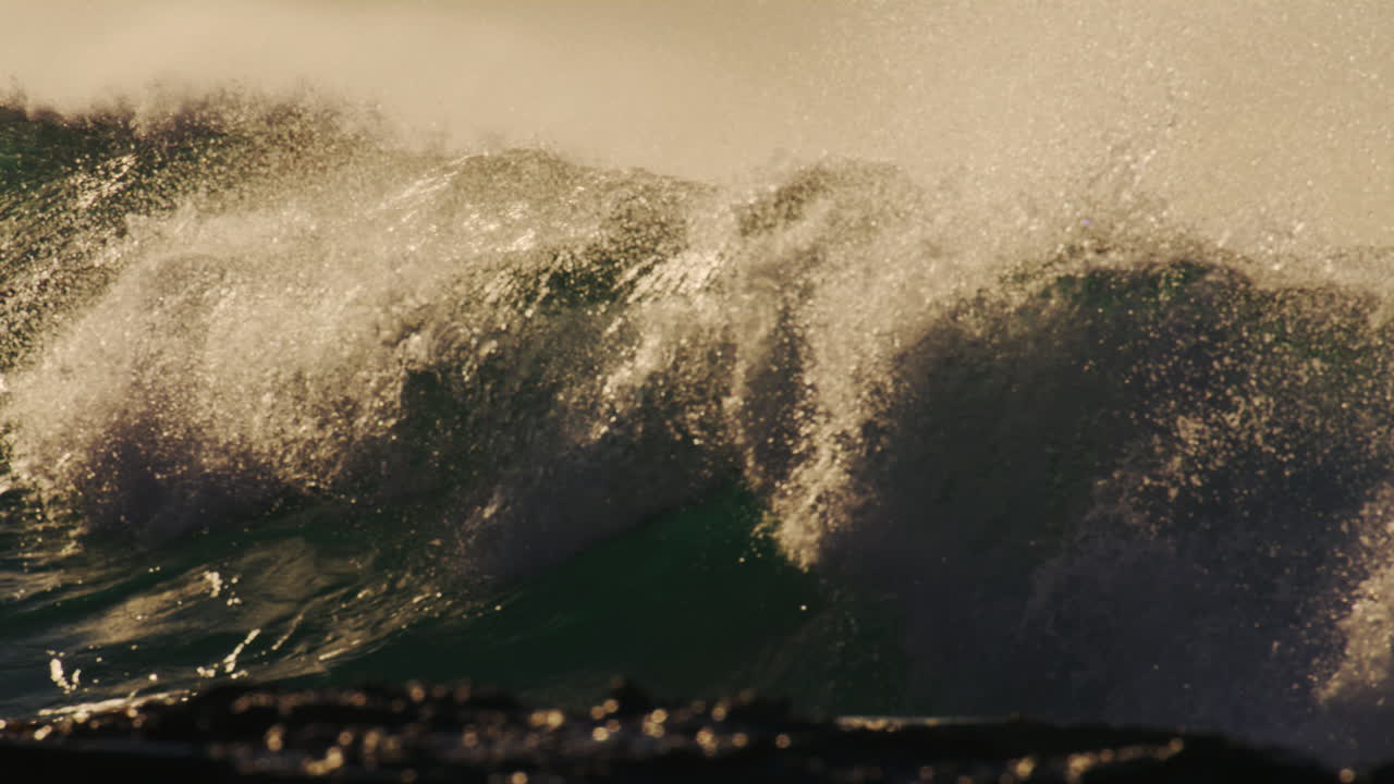 Slow motion view of surfer at golden hour, golden sky illuminated against sparkling blue and white foam of waves