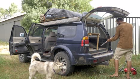 man with dog vacuuming inside of dirty suv cleaning vehicle after road trip