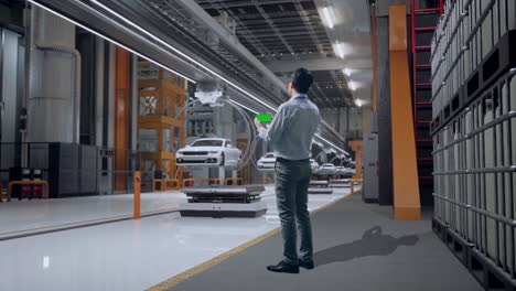 full body back view of an asian male professional worker standing with green screen smartphone in ev car factory, high-tech industrial facility