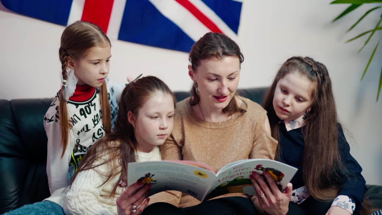 Teacher and schoolgirls on the sofa in class. Young female teacher reading a book to children while sitting together on the couch at school. Elementary education concept.