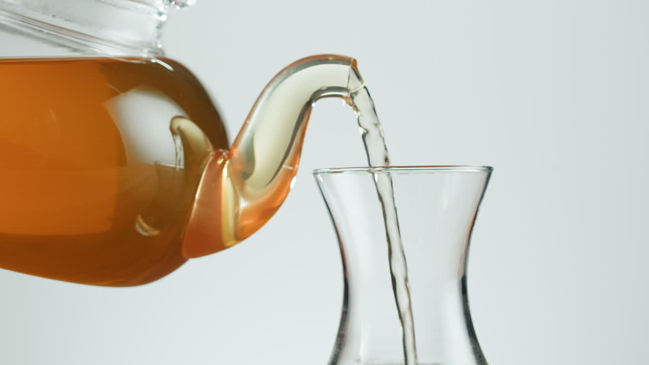 Tea being poured from a glass teapot into a glass