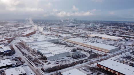 Epische-Winteraufnahme-Des-Industriegebiets-Aus-Der-Luft-Mit-Dampfenden-Dächern-Und-Der-Innenstadt-Im-Hintergrund