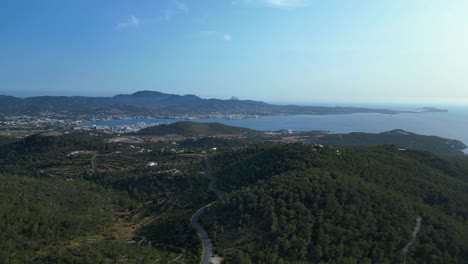 road winding through a vibrant green forest in ibiza, spain, leading down towards the beautiful san antonio bay. nice aerial view flight panorama overview drone