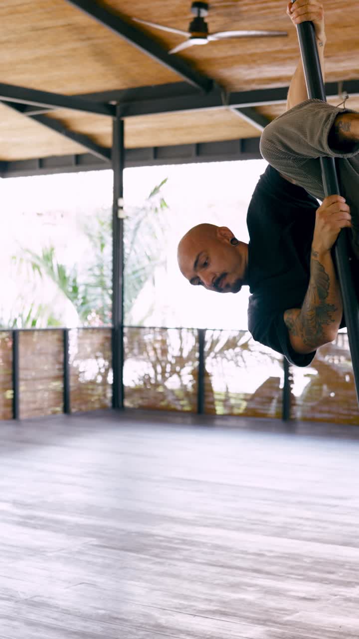 Uomo atletico che esegue esercizi di pole fitness in uno studio moderno
