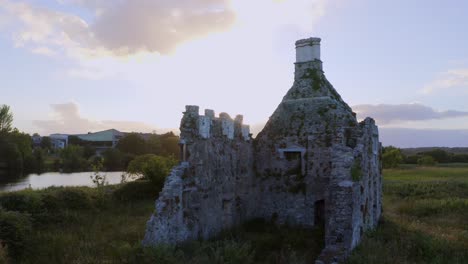 Slow-aerial-pan-right-across-Terryland-Castle-on-River-Corrib,-Galway-Ireland-as-sun-flare-blooms