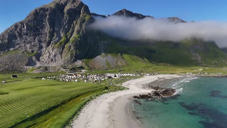 flakstad beach in lofoten, drone view, mountain covered in white clouds, white sand beach and full campsite