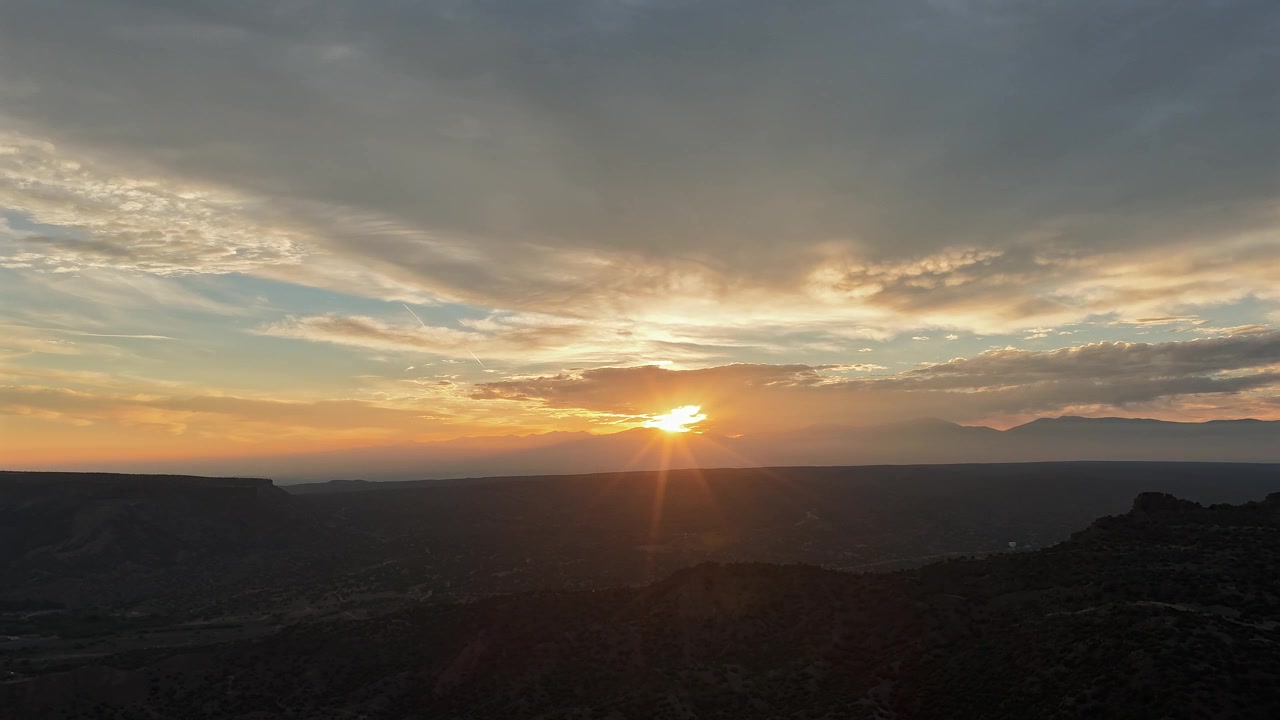 Hyperlapse aereo 4K di un'alba radiosa su un profondo canyon sud-occidentale. Raggi di sole dorati filtrano tra le nuvole mattutine, illuminando un orizzonte montuoso sfocato e in silhouette in lontananza
