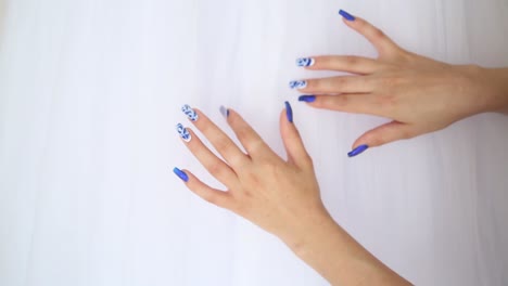 woman's hands with decorated blue nails on a white dress