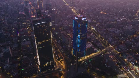 Aerial-hyperlapse-of-skyscraper-flashing-lights-as-cars-zoom-by-at-night,-Mexico-City