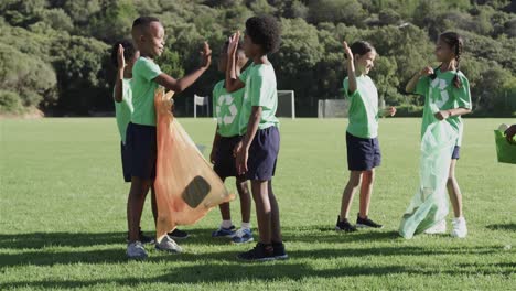 Happy-diverse-schoolchildren-high-fiving-and-cleaning-sports-field-at-elementary-school