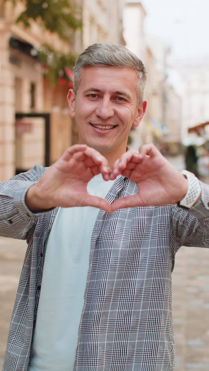 Caucasian man makes symbol of love showing heart sign express romantic feelings on city street