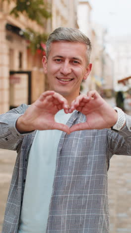 caucasian man makes symbol of love showing heart sign express romantic feelings on city street