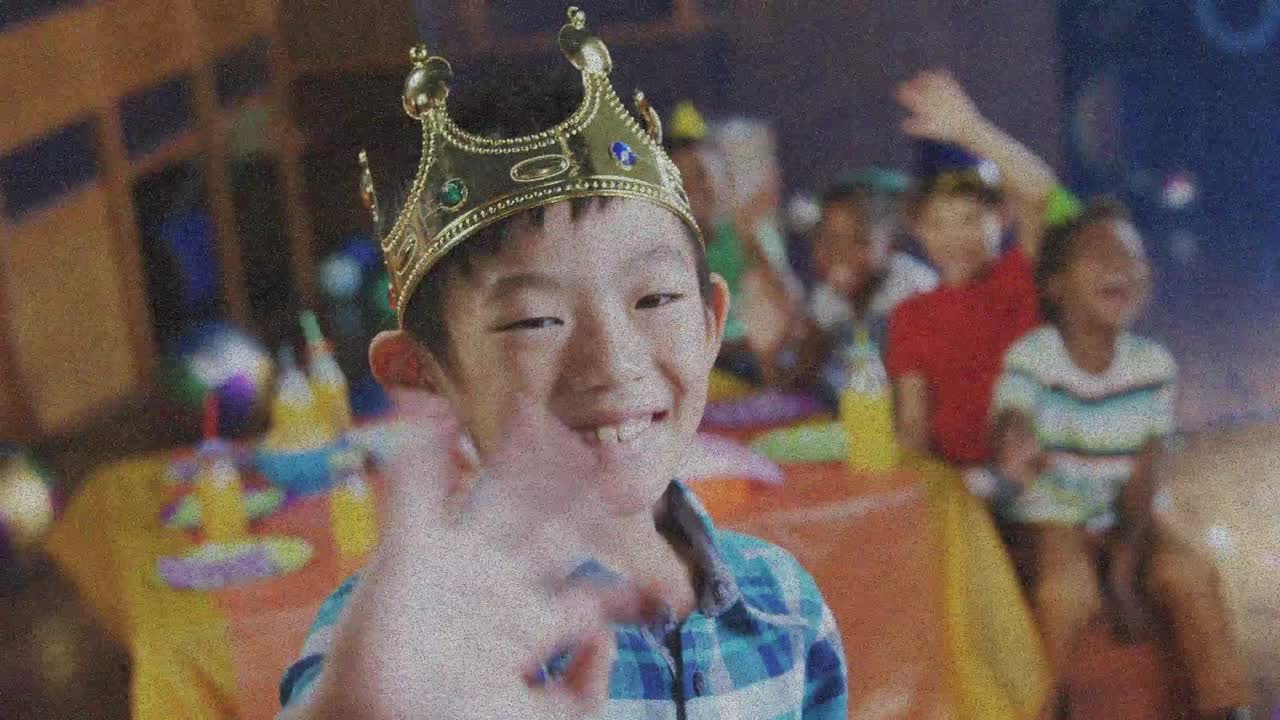 パーティーで楽しむ多国籍の友達と、王冠をかぶって挨拶するアジア人男の子のアニメーション。