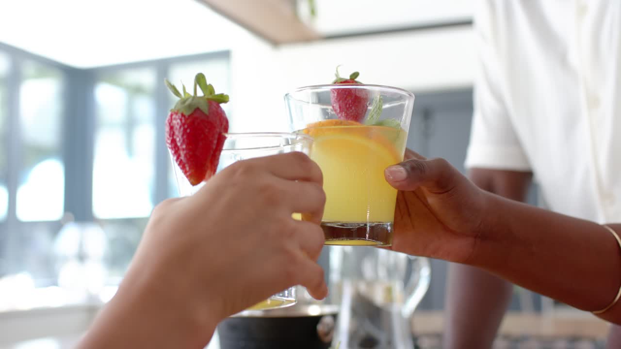 Hands are reaching from sides, aligning garnished citrus glasses on wooden counter for shared toast
