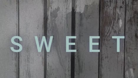 animation of sweet text over looping abstract pattern against wooden wall in background