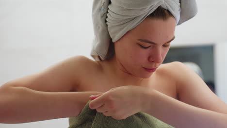 portrait view of young woman tightening towel on her chest after shower in bathroom, natural lighting highlights smooth skin, close-up of gentle action as towel is adjusted