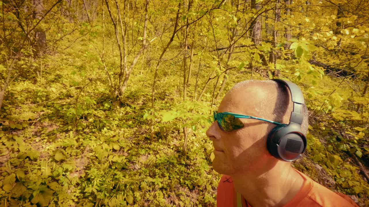 A modern mature man in his 50s using wireless headphones and sunglasses while hiking. Intersection of technology, gadgets, and active outdoor lifestyle. 4k quality
