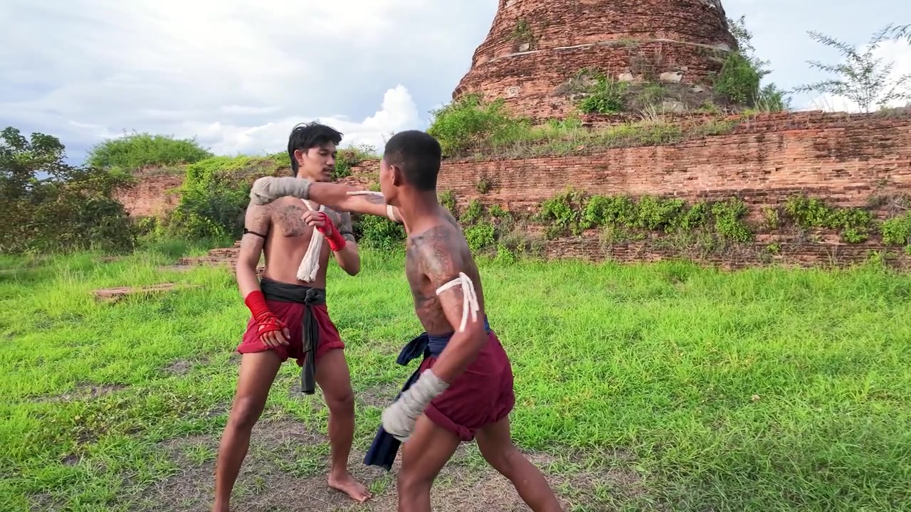Two traditional Thai boxers practice martial arts outdoors near historic temple ruins in Ayutthaya, Thailand.