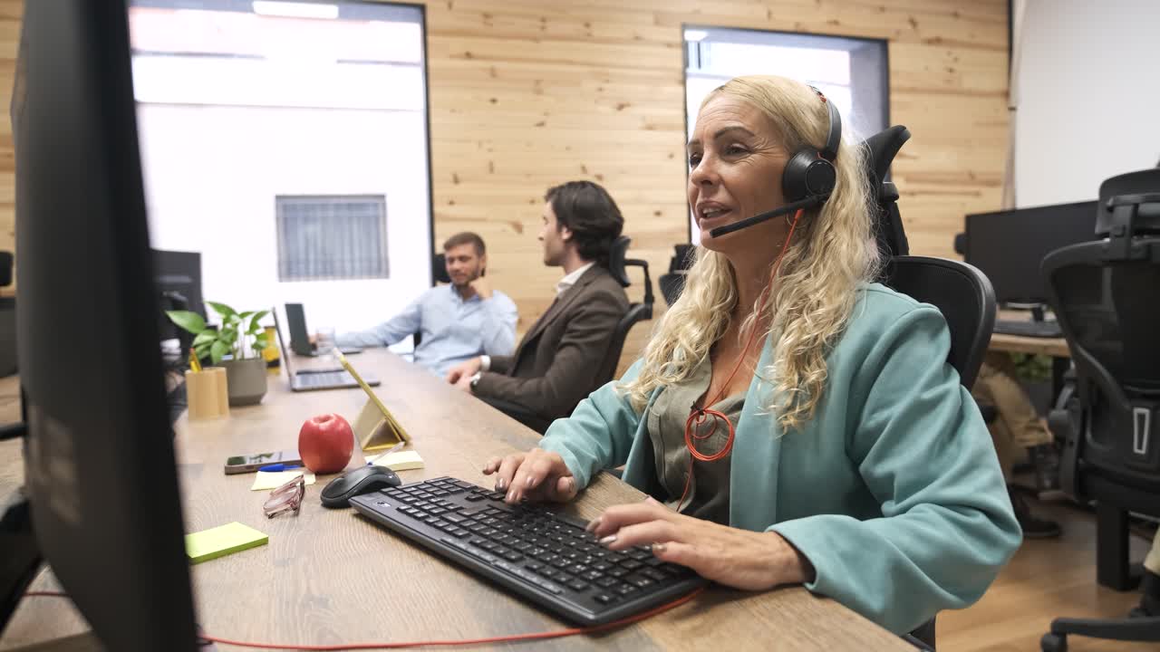 Happy mature businesswoman talking as she wears headset in coworking office