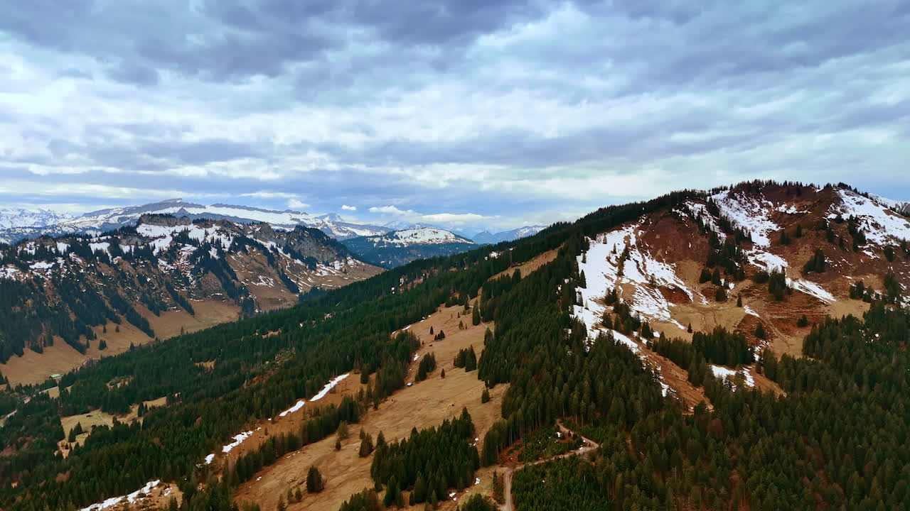 Dramatic cloudscape covering the horizon over the mountainous landscape. Aerial view on the snow-capped rocks wooded with pine trees.