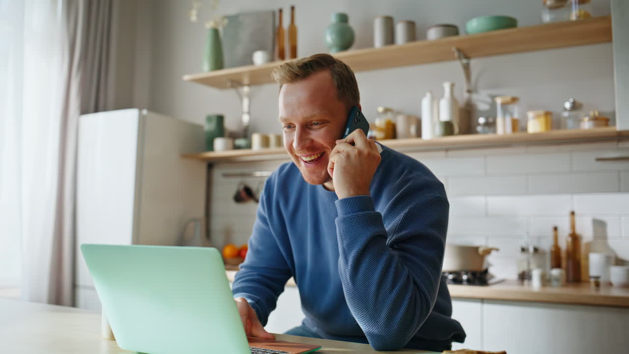 Glad freelancer taler i mobiltelefon, kigger på bærbar computer, drikker kaffe – nærbillede.