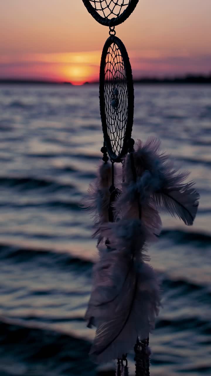Acchiappasogni con piume che ondeggiano dolcemente contro un tramonto sull'acqua